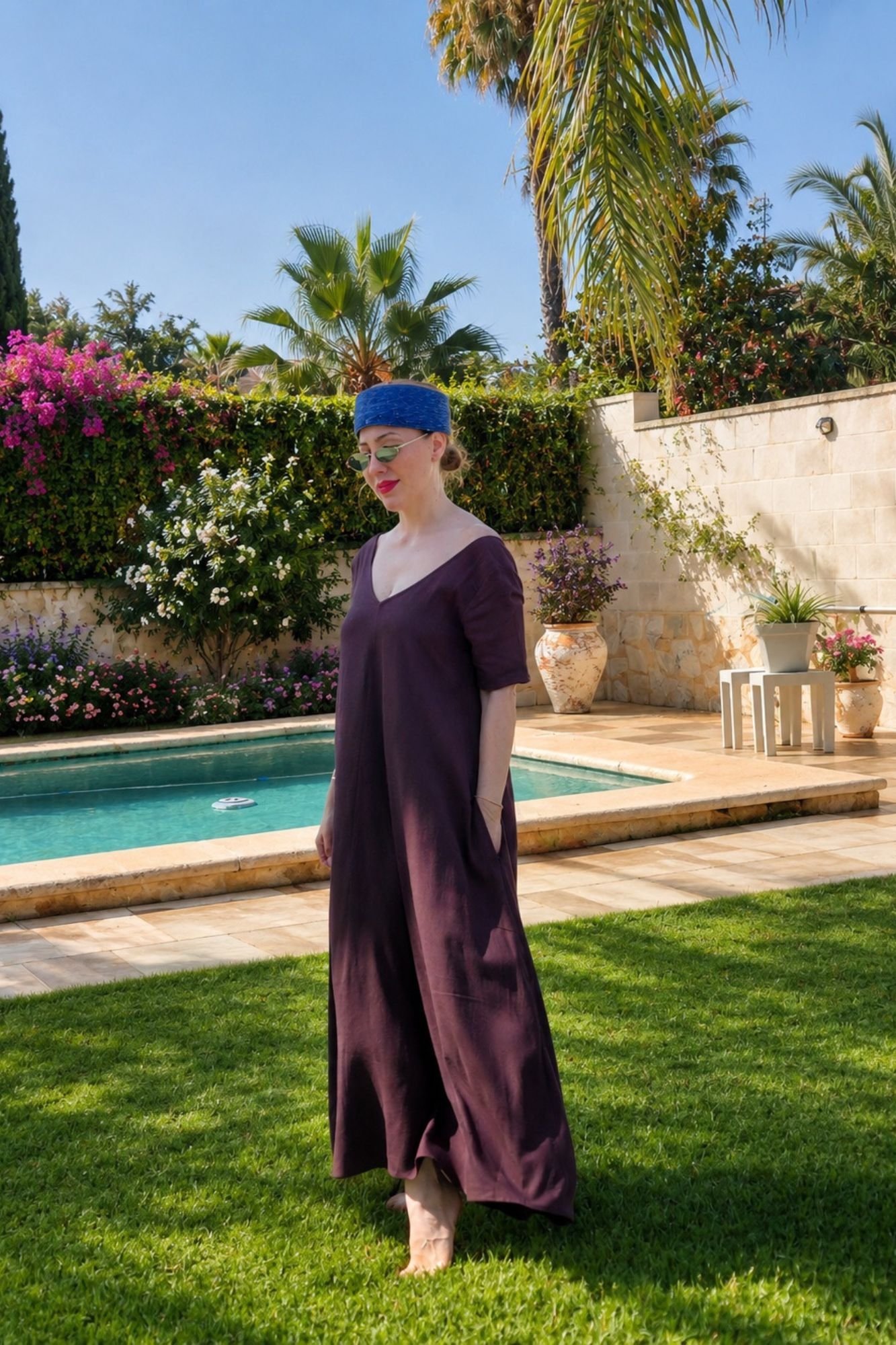 1 Mujer posando en un jardín con piscina luciendo un vestido largo fluido de color marrón chocolate con doble escote en V y manga corta, de la marca OH.LA.
