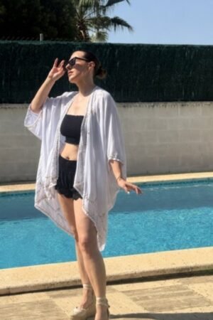 Mujer luciendo el caftán Irun de OH.LA en tono claro con bordados dorados y bajo redondeado junto a una piscina.
